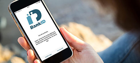En person som är bekvämt placerad hemma, eller "hemma", håller en smartphone som visar BankID-appens skärm för inloggnings- eller identifieringssyfte.