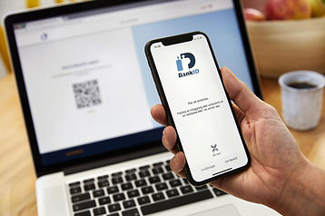 En person håller en smartphone som visar BankID-appen nära en öppen bärbar dator som visar en QR-kod på skärmen, redo för sömlös tillgång till digitala tjänster med datorhjälp hemma.