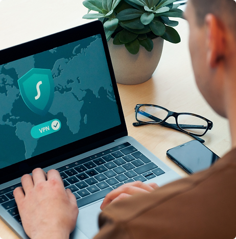 En person som är uppslukad av IT-Säkerhet använder en bärbar dator som visar ett VPN-gränssnitt. I närheten vilar glasögon bredvid en smartphone och en krukväxt pryder det städade skrivbordet.